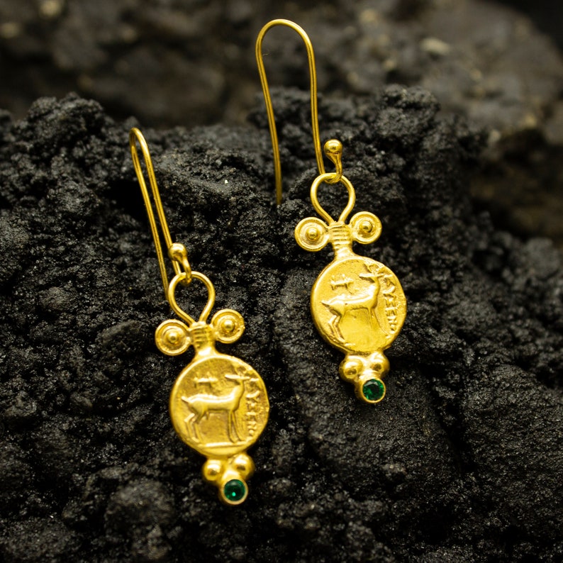 Pu&ograve; includere: Orecchini dorati con un designo a forma di cervo e accenti di pietre preziose verdi. Gli orecchini sono di stile pendente con un anello nella parte superiore per appendere.