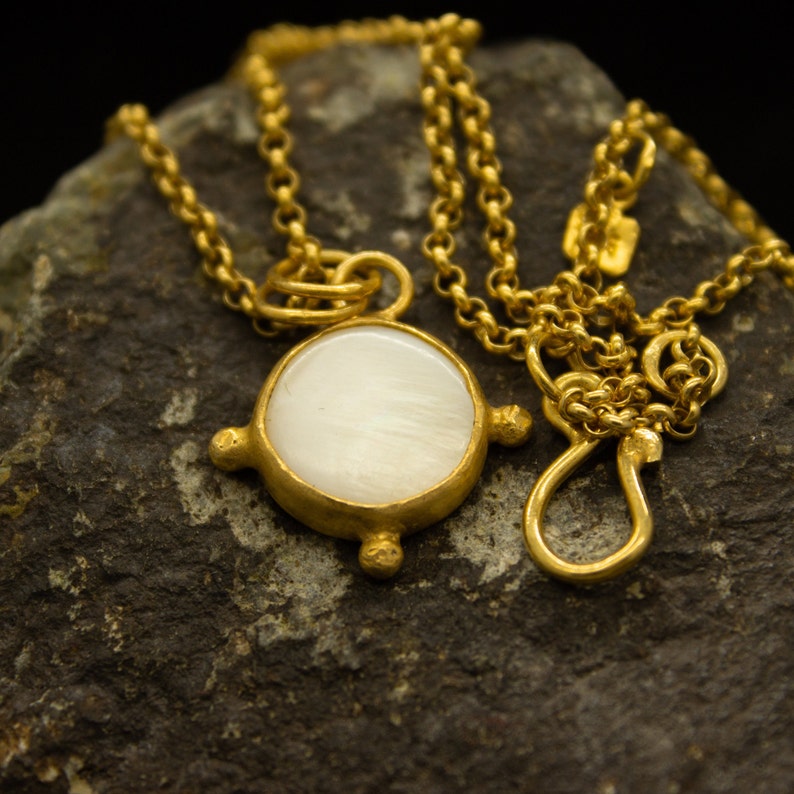May include: A gold chain necklace with a round white pendant. The pendant has a textured edge and a smooth, white surface.