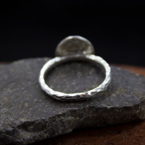 Op de afbeelding: Een zilveren ring met een gehamerde afwerking. De ring ligt op een grijze steen.