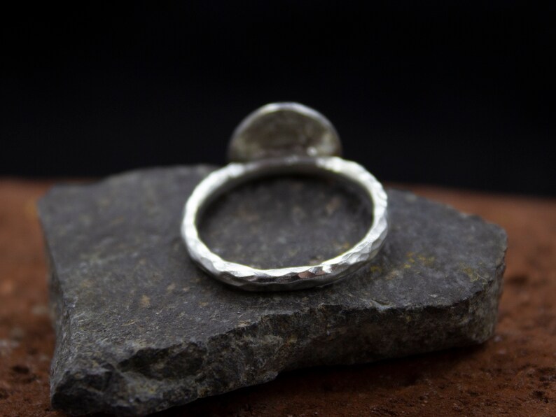 Op de afbeelding: Een zilveren ring met een gehamerde afwerking. De ring ligt op een grijze steen.