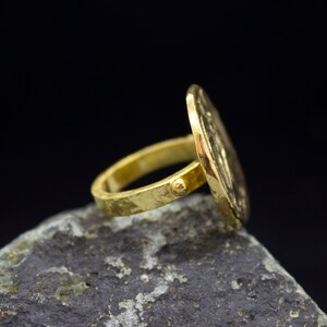 Peut inclure: Une bague en or avec un dessus rond et textur&eacute;. La bague est pos&eacute;e sur une roche grise.