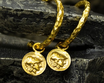 May include: Gold hoop earrings with a textured finish and a dangling coin charm featuring a profile of a person wearing a helmet.