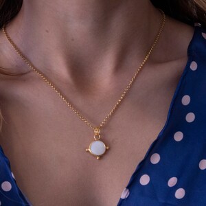May include: A gold chain necklace with a white round pendant. The pendant has a gold border and four small gold points.