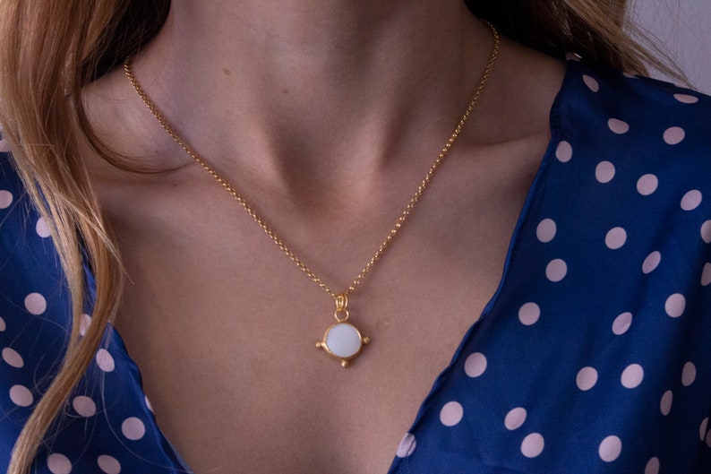 May include: A gold chain necklace with a white round pendant. The pendant has a gold border and four small gold points.