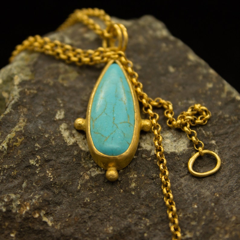 May include: A turquoise gemstone pendant with a gold chain. The pendant is shaped like a teardrop and has a textured surface. The chain is made of small, linked gold circles.