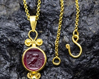 May include: Gold necklace with a red cameo pendant featuring an owl and the inscription "AΘE". The pendant is surrounded by gold beads and a green gemstone.