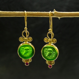 May include: Gold earrings with green glass owl charms and pink gemstones. The owls are in a cameo-like design.