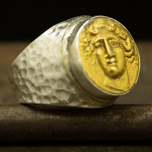 Puede incluir: Un anillo de plata con textura martillada y una parte superior de forma de moneda de oro que presenta un perfil detallado de la cara de una mujer.