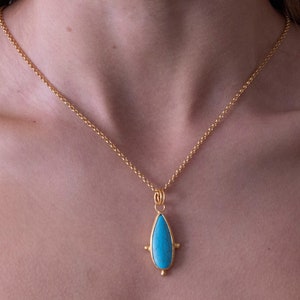 May include: A gold chain necklace with a turquoise teardrop pendant. The pendant has a gold setting with four small gold balls around the stone.