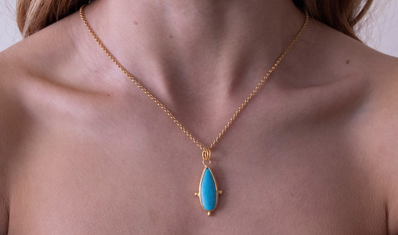 May include: A gold chain necklace with a turquoise teardrop pendant. The pendant has a gold setting with four small gold balls around the stone.