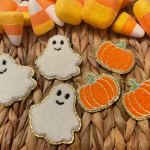 May include: Five felt Halloween decorations: three white ghosts with black eyes and mouths, and two orange pumpkins with green stems.