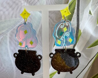 May include: A pair of black glitter cauldron earrings with iridescent blue and pink cloud charms. The charms have yellow glitter stars.