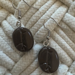 May include: A pair of silver dangle earrings with brown coffee bean shaped charms.