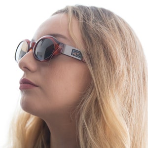 May include: A woman wearing brown and silver oval sunglasses with a reflective lens. The sunglasses have a silver frame and a brown tortoise shell pattern.