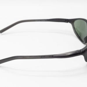 May include: Black sunglasses with green lenses. The sunglasses have a curved frame and a thin, flexible arm.