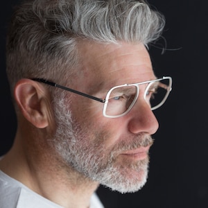 Puede incluir: Un hombre con cabello gris y barba que lleva gafas con montura plateada. Est&aacute; mirando hacia la derecha del encuadre.