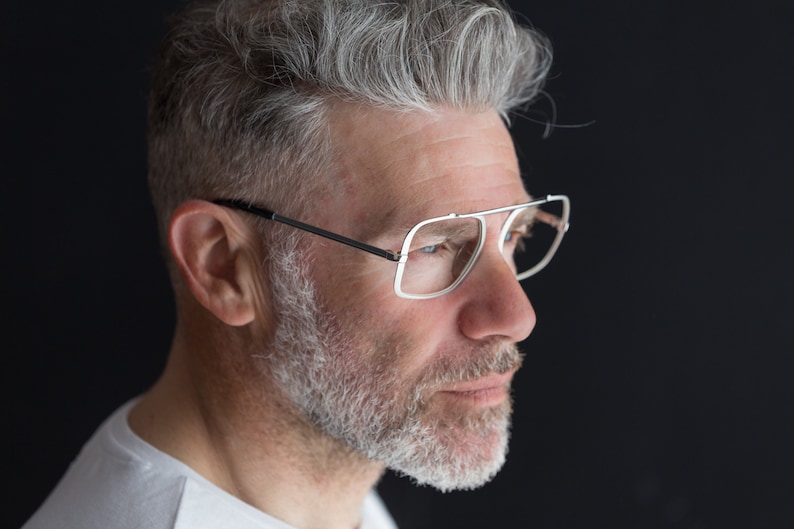 Puede incluir: Un hombre con cabello gris y barba que lleva gafas con montura plateada. Est&aacute; mirando hacia la derecha del encuadre.