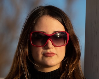 Puede incluir: Una mujer con el pelo largo y castaño que lleva gafas de sol rojas.