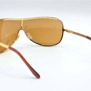 May include: Gold-tone aviator sunglasses with brown lenses and brown temples. The sunglasses have a Versace logo on the side.