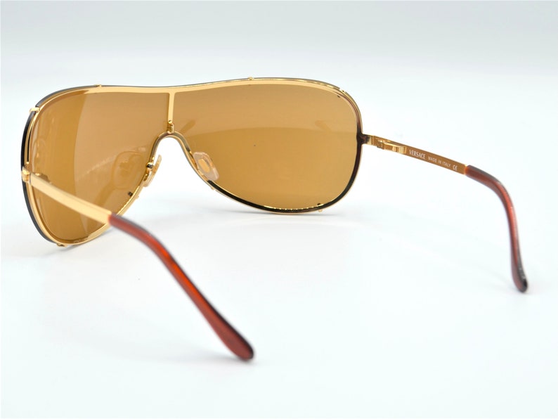 May include: Gold-tone aviator sunglasses with brown lenses and brown temples. The sunglasses have a Versace logo on the side.