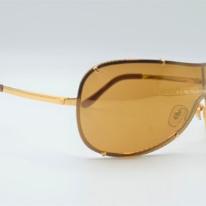 May include: Gold-tone aviator sunglasses with brown lenses and a curved frame.