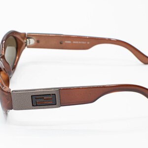 May include: Brown plastic sunglasses with a silver metal accent on the side featuring the letter "F".