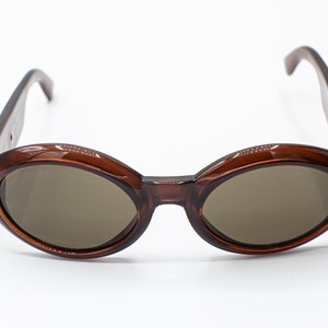 May include: Brown oval-shaped sunglasses with brown lenses. The sunglasses have a simple design with no embellishments.