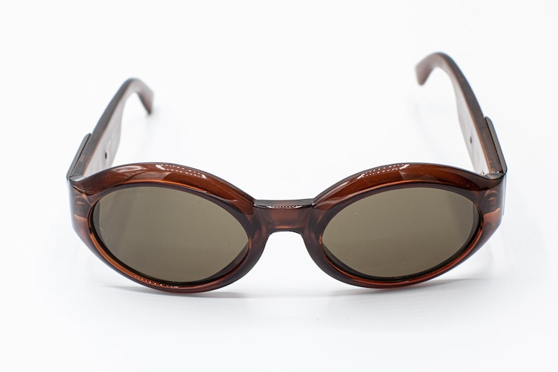 May include: Brown oval-shaped sunglasses with brown lenses. The sunglasses have a simple design with no embellishments.