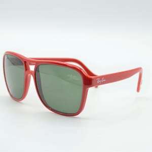 May include: Red Ray-Ban sunglasses with green lenses. The sunglasses have a classic aviator style frame.