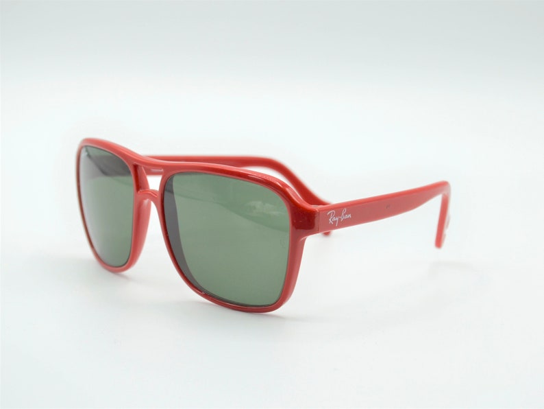 May include: Red Ray-Ban sunglasses with green lenses. The sunglasses have a classic aviator style frame.