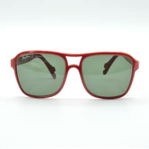 May include: Red plastic aviator sunglasses with green lenses. The sunglasses have the Ray-Ban logo on the left lens.