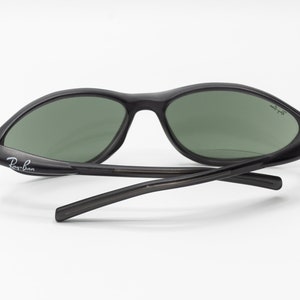 May include: Black Ray-Ban sunglasses with green lenses. The sunglasses have a curved frame and a thin, black temple.