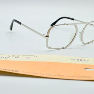 Puede incluir: Gafas de metal plateadas con patillas de pl&aacute;stico negro. Las gafas tienen una montura rectangular con una forma ligeramente cuadrada. La etiqueta en la parte inferior dice "W 5025" y "exquisit in Qualitat und Design".