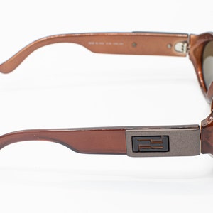 May include: Brown plastic sunglasses with a silver metal accent on the side featuring the letter "F".
