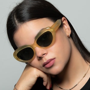 May include: A woman wearing yellow cat-eye sunglasses with dark lenses. The sunglasses have a translucent yellow frame.