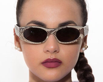May include: A woman wearing a pair of oval-shaped sunglasses with a brown and white snakeskin pattern. The sunglasses have dark lenses.