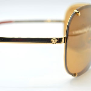 May include: Gold-tone aviator sunglasses with brown lenses and a Versace logo on the arm.