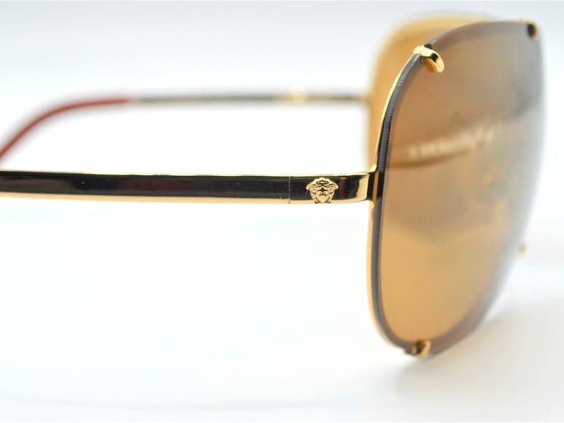 May include: Gold-tone aviator sunglasses with brown lenses and a Versace logo on the arm.