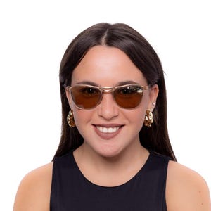 May include: Gold-framed sunglasses with brown lenses. The sunglasses have a classic design with a double bridge and a rectangular shape. The person is wearing gold-toned earrings and a black top.