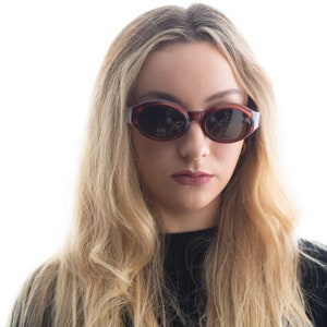 May include: A woman with long blonde hair wearing brown oval sunglasses. She is wearing a black shirt.