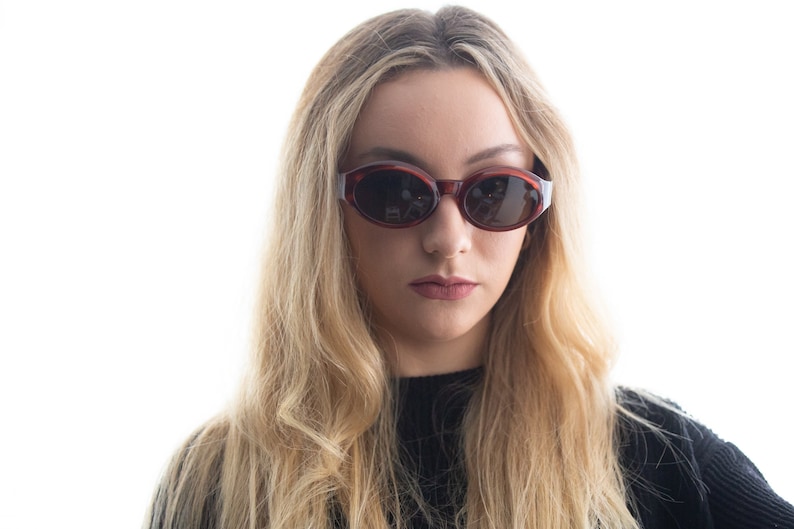 May include: A woman with long blonde hair wearing brown oval sunglasses. She is wearing a black shirt.