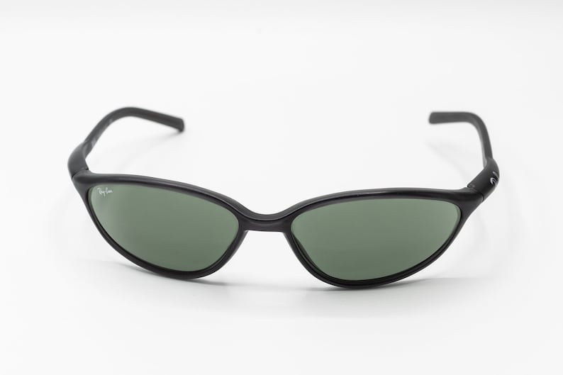 May include: Black Ray-Ban sunglasses with green lenses. The sunglasses have a thin, curved frame and a Ray-Ban logo on the side.