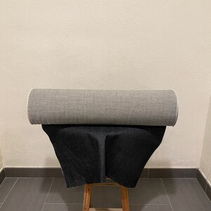 May include: A roll of gray fabric and a roll of black fabric are displayed on a wooden stool. The fabric is folded and placed on top of the stool.