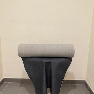 Könnte beinhalten: Eine Rolle grauer Stoff liegt auf einer Rolle schwarzen Stoffes. Beide Rollen stehen auf einem Holzhocker.