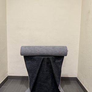 May include: A roll of dark blue fabric with a light blue and pink patterned backing. The fabric is rolled up and sitting on a gray tiled floor.