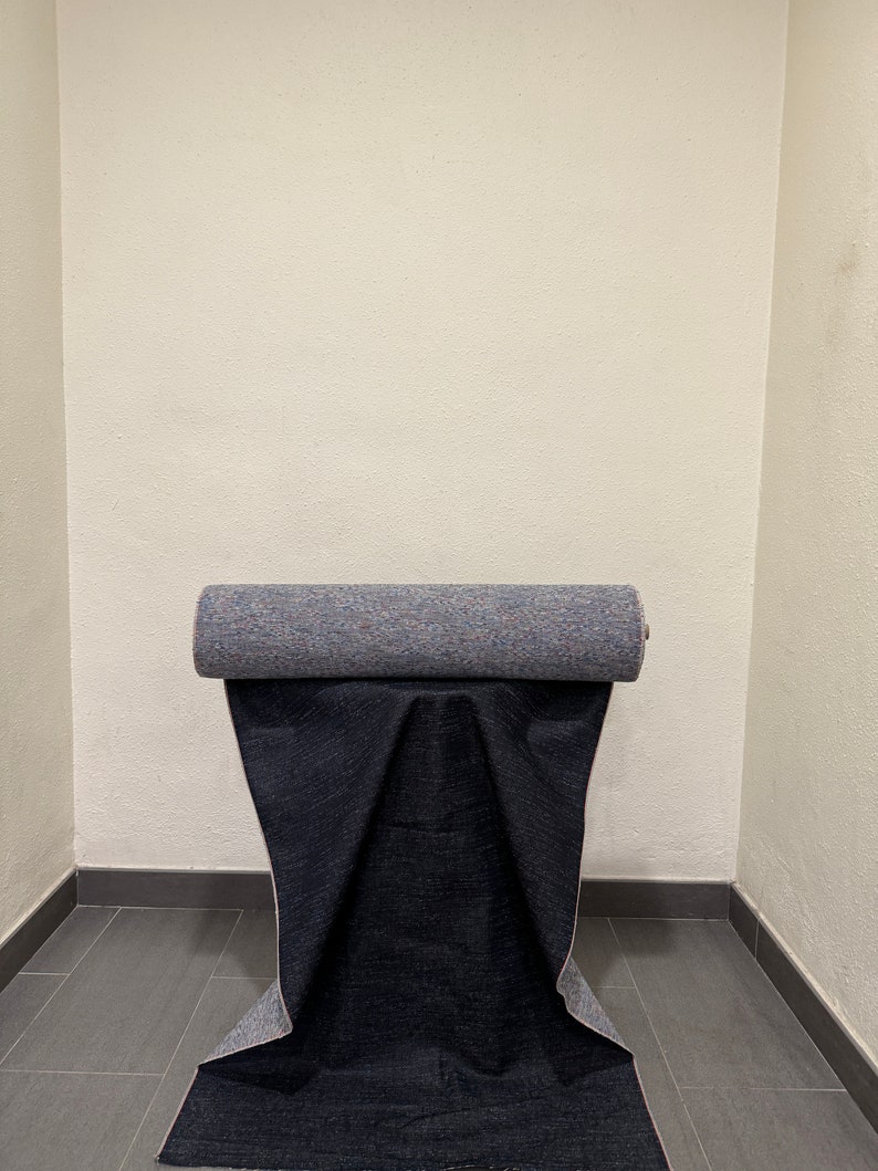 May include: A roll of dark blue fabric with a light blue and pink patterned backing. The fabric is rolled up and sitting on a gray tiled floor.