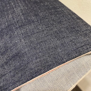 Könnte beinhalten: Nahaufnahme eines dunkelblauen Jeansstoffes mit rotem Selvedge-Rand. Der Stoff ist umgeklappt, um die weiße Unterseite zu zeigen.
