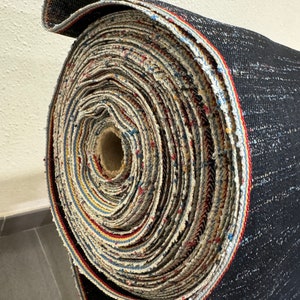 May include: A roll of black fabric with a multi-colored trim. The fabric is rolled up tightly and the trim is visible on the outside of the roll.