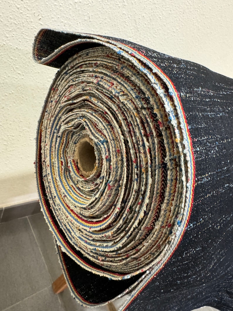 May include: A roll of black fabric with a multi-colored trim. The fabric is rolled up tightly and the trim is visible on the outside of the roll.