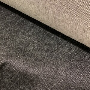May include: Two pieces of denim fabric, one light gray and one dark gray, are shown side by side. The fabric has a woven texture.